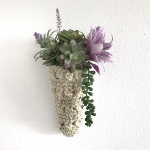 a photo of a cone shaped plant hanger hanging on the wall. it hold succulents with bright green and lavender tones.