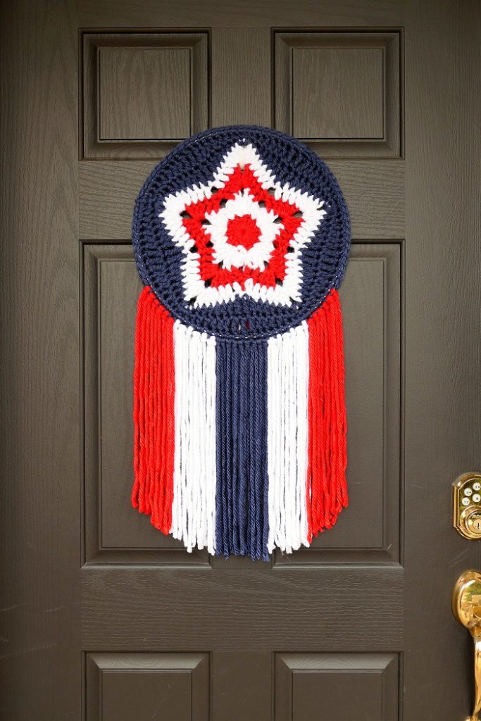 A red, white, and blue granny star mandala hanging on a black door to celebrate the 4th of July